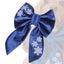 A blue velvet bow with white snowflake designs, featuring a dog in the background.